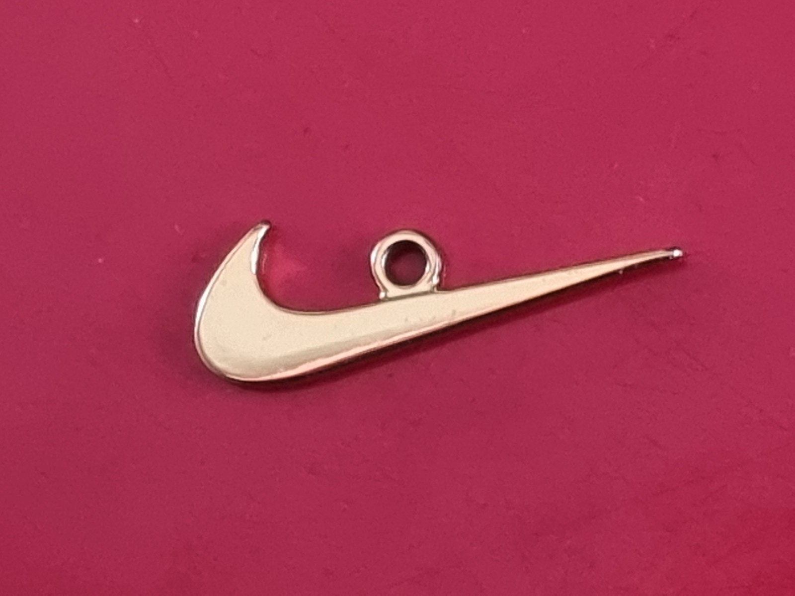 Small Nike tick pendant. Gold-coloured
