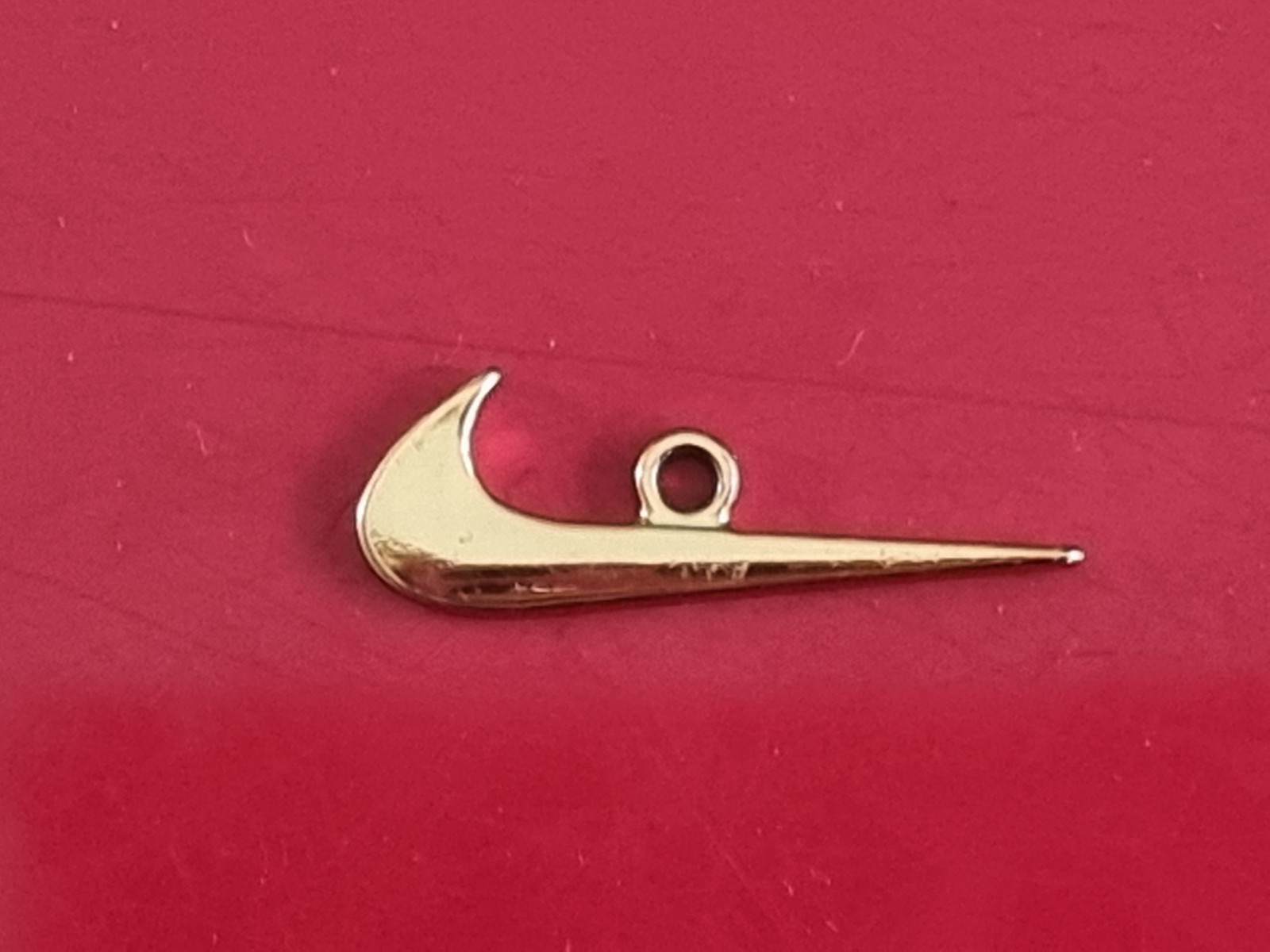 Small Nike tick pendant. Gold-coloured